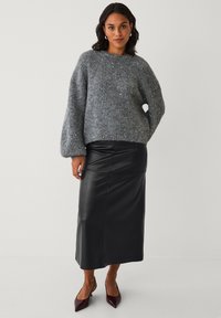 Grauer Strickpullover mit rundem Ausschnitt und strukturiertem Finish. Kombiniert mit einem schwarzen Leder-Maxirock und burgunderroten Pumps mit spitzer Spitze.