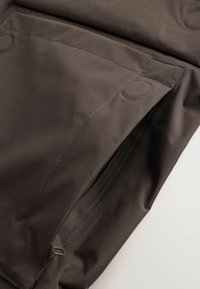 Gros plan sur un tissu foncé avec une fermeture éclair imperméable partiellement ouverte et un détail de couture renforcée.