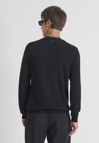 Maglione nero a maglia con colletto rotondo, dettagli a costine sulle maniche e una superficie liscia. Indossato con pantaloni scuri, visto da dietro.