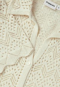Gräddfärgad cardigan med intrikata stickade mönster, som har en texturerad yta, knappstängning och en vikkrage.