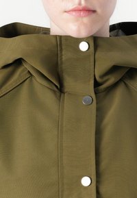 Olive green jacket with a high collar, featuring a metal snap closure and visible stitching details, made from smooth, textured fabric.