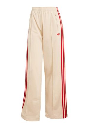 Beige wide-leg track pants with elastic waistband, red side stripes, zippered pocket, and red Adidas Trefoil logo on the right thigh.