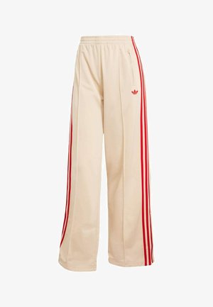 Beige trackbukser med vide ben, elastisk talje, røde sidestriber, lynlås-lomme og rødt Adidas Trefoil-logo på højre lår.