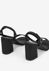 Sandali neri con tacco alto, dotati di tomaia in tessuto, cinturino alla caviglia con fibbia silver e un tacco a blocco spesso per garantire stabilità.