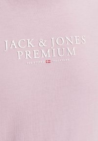 Šviesiai rožinė marškinė su baltais reljefiniais užrašais "JACK & JONES PREMIUM" ir registracijos ženklu, taip pat su Danijos vėliavos akcentu.