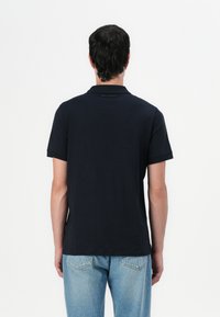 Mornarsko pametno polo majica z umetno ovratnikom in kratkimi rokavi, z diskretnim logotipom na hrbtni strani in sproščenim krojem.