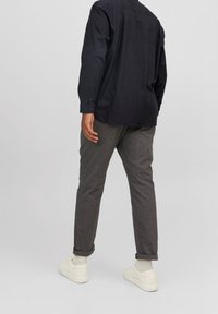 Camisa de botón de manga larga oscura combinada con pantalones grises ajustados, con puños remangados y zapatillas blancas para un look casual.