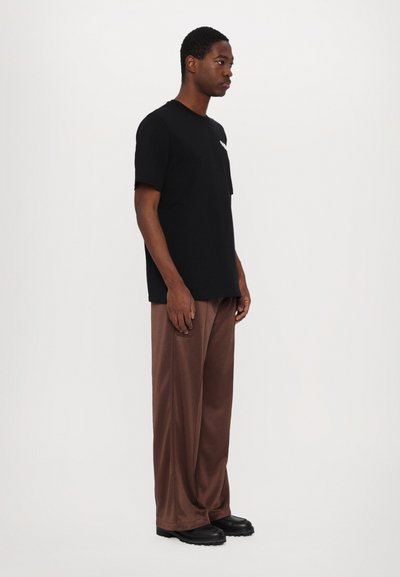 Camiseta de algodón negra con cuello redondo, combinada con pantalones marrones holgados y zapatos negros; diseño liso sin patrones visibles.