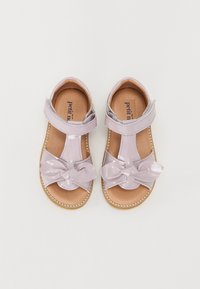 Sandales en cuir verni lavande avec un détail en nœud, une sangle de cheville réglable et un intérieur beige. Présente des coutures sur la semelle.