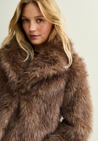 Manteau en fausse fourrure marron avec une texture douce, un col large et des manches oversize. La couleur riche présente des variations subtiles pour plus de profondeur.