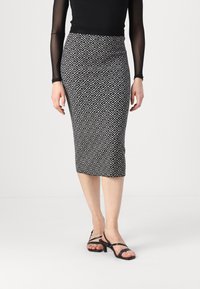 Jupe crayon noire et blanche à motifs géométriques, de longueur genoux, accompagnée de talons noirs à lanières. Tissu doux et extensible.