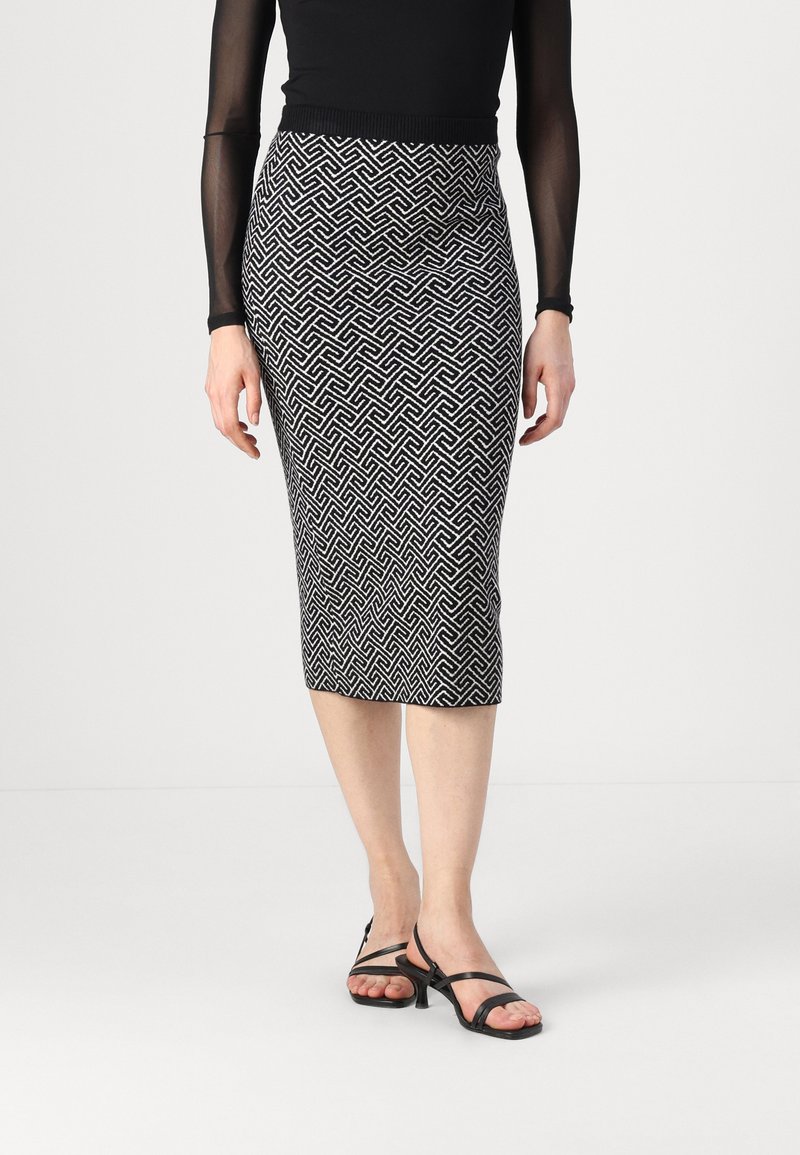 Jupe crayon noire et blanche à motifs géométriques, de longueur genoux, accompagnée de talons noirs à lanières. Tissu doux et extensible.
