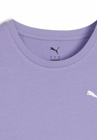 T-shirt viola in cotone a girocollo con logo Puma bianco, texture liscia e etichetta con informazioni sulla taglia e le istruzioni di cura.
