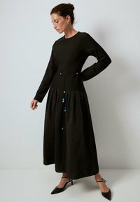 Pitkä musta mekko, jossa on tiukka yläosa ja levenevä hame. Tässä on naru-akseli, jossa on sinisiä helmiä. Valmistettu tekstuurikankaasta.