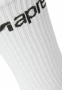 Weiße gerippte Socke mit schwarzem gesticktem Markentext. Das Material wirkt weich mit einem leichten Glanz und gleichmäßiger Textur insgesamt.