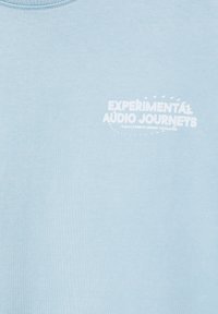 Tissu bleu clair avec texte blanc indiquant "Experimental Audio Journeys" et texte plus petit et moins lisible en dessous, en haut à gauche.