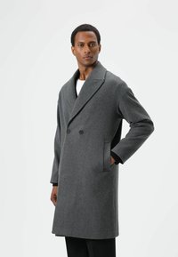 Grijze wollen jas met een dubbelbreasted ontwerp, brede revers, zijzakken en contrasterende zwarte manchetten.