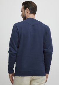 Felpa blu navy con collo rotondo, maniche lunghe e polsini a coste. Il tessuto appare liscio con una sottile trama.