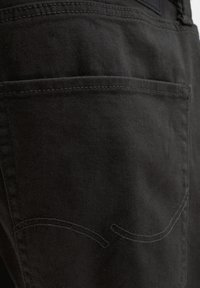 Fekete farmeranyag közeli felvétele, amely a dupla varrással és finom ívelt varrásdíszítéssel ellátott hátsó zsebet mutatja.