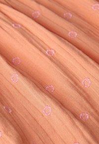 Pfirsichfarbener Stoff mit einer weichen Textur, der rosa gestickte Blumen in einem verstreuten Muster und subtile vertikale Falten aufweist.