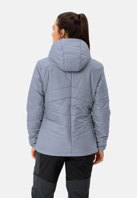 Giacca imbottita di un grigio chiaro con cappuccio, caratterizzata da cuciture verticali e orlo dritto. L'interno ha una texture liscia.