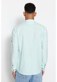 Camicia a maniche lunghe verde menta chiaro realizzata in un tessuto testurizzato. Presenta bottoni neri ai polsini e un design della yoke posteriore con spacco.