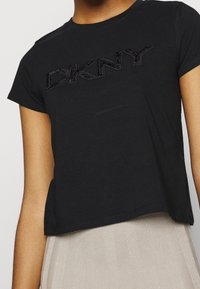 T-shirt nera a maniche corte in cotone, con logo DKNY testurizzato in un design nero leggermente in rilievo. Vestibilità corta, tessuto morbido.
