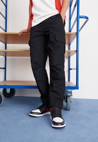 Black cargo pants with a straight fit, featuring side pockets and a smooth texture, paired with black and white sneakers.