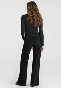 Zwarte high-waisted wijde jeans met een zachte textuur, achterzakken en subtiele stikdetails, gecombineerd met een aansluitend zwart topje.