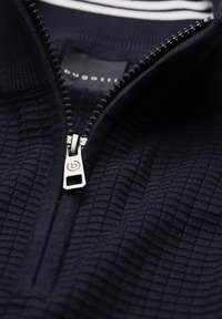 Marineblaue Zip-Up-Strickjacke aus strukturiertem Stoff mit Karomuster, einem Metallreißverschluss und einem schwarzen Etikett im Kragen.