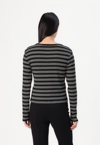 Svart-hvite striper langermet topp med rund hals; tettsittende design og myk stoff; ensfarget bak uten ekstra detaljer.