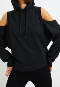 Zwarte hoodie met uitsnijdingen op de schouders, gemaakt van een zachte, textuurstof. Voorzien van trekkoorden en een relaxte pasvorm.