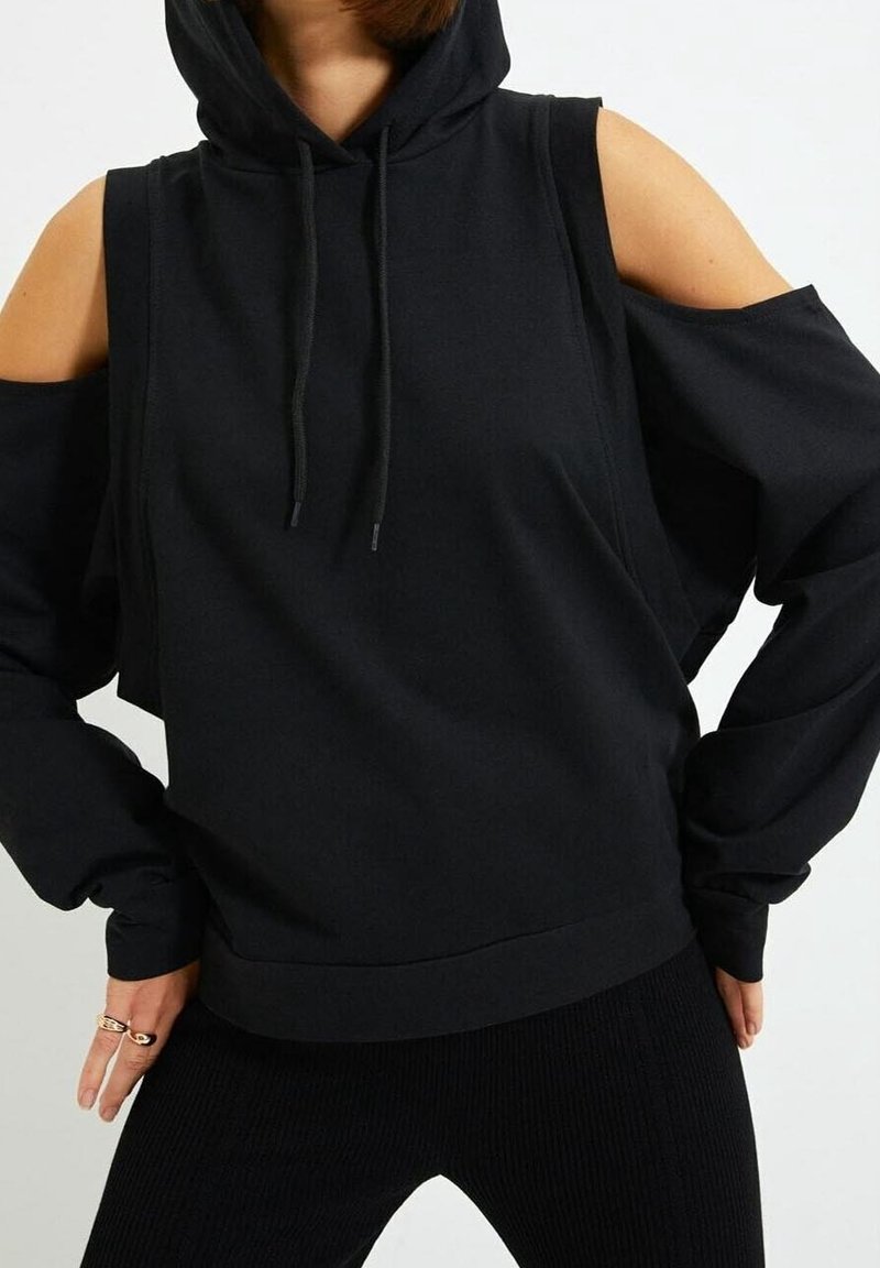 Zwarte hoodie met uitsnijdingen op de schouders, gemaakt van een zachte, textuurstof. Voorzien van trekkoorden en een relaxte pasvorm.