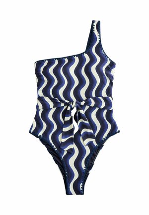 Frau trägt einen Badeanzug mit einem Träger und marineblauen und weißen wellenförmigen Streifen, von hinten vor einem unscharfen Außenhintergrund gezeigt.