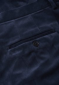 Krupan plan tamnoplave baršunaste tkanine s jednim crnim dugmetom ušivenim blizu mulja džepa.