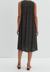 Mustaton hihaton mekko, jossa on valkoinen pilkku-kuvio, laaja design ja kevyt kangas, polvipituinen leikkaus ja lievää poimutusta.