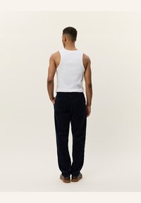 Un maiou alb asortat cu pantaloni din catifea cord de culoare albastru închis. Outfitul are o croială lejeră și detalii la buzunarele din spate.