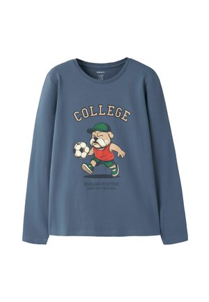 Chemise bleue à manches longues avec un chien de dessin animé portant une casquette et jouant au football, texte "COLLEGE" au-dessus et petit texte sous le chien.
