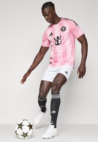 Rosa stribet fodboldtrøje med sorte accenter, hvide shorts, sorte fodboldsokker og hvide fodboldstøvler; spiller interagerer med en mønstret bold.