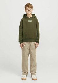 Grön huvtröja med framficka och logotypemblem, kombinerad med beiga cargobyxor med sidofickor och avslappnad passform. Vita sneakers med detaljer.