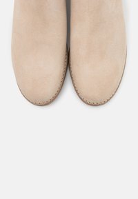 Stivaletti alla caviglia in suede beige con punta arrotondata, texture liscia e cuciture visibili lungo la suola. Nessun hardware o motivi aggiuntivi.