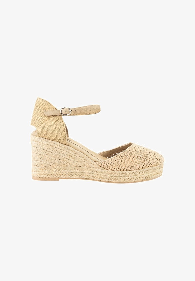 Espadrille de cuña en beige con parte superior de lona tejida y suela de yute texturizada. Cuenta con una correa en el tobillo con una hebilla plateada.