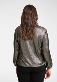 Top scuro metallizzato con maniche lunghe, caratterizzato da una texture liscia e lucida e polsini arricciati. Sfondo bianco uniforme.