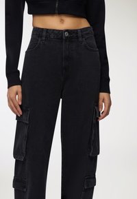 Czarne dżinsowe spodnie cargo o luźnym kroju, z bocznymi kieszeniami, zapięciem na guzik oraz fakturowanym materiałem.