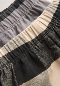 Ternet stof med et farveskema i grå, sort og beige. Har elastiske linninger og en blød tekstur med en let glans.