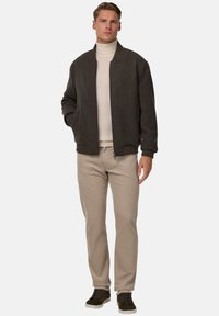 Tmavě šedá bomber bunda s vysokým límcem, béžový rolák pod ním, světlé béžové kalhoty a tmavozelené tenisky. Hladká textura, neformální styl.