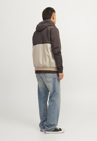 Hooded jacket with gray top half and beige bottom half, featuring elastic cuffs and a drawstring hem, paired with light blue jeans and black sneakers.