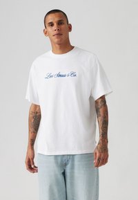 Weißes Baumwoll-T-Shirt mit blauem gesticktem "Levi Strauss & Co." Logo. Lockerer Schnitt, runder Ausschnitt, kurze Ärmel, glatte Textur.