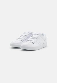 Baskets blanches avec une tige en cuir lisse, bout perforé pour la respirabilité, lacets plats et semelle en caoutchouc texturé. Marquage minimal sur le côté.