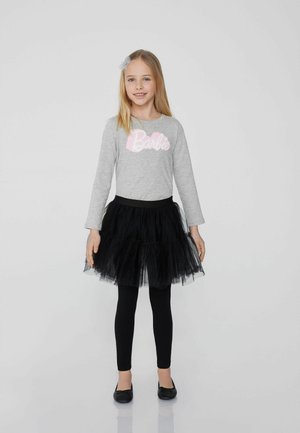 Graues Langarmshirt mit pinkem "Barbie"-Logo, kombiniert mit einem geschichteten schwarzen Tüllrock, schwarzen Leggings und schwarzen Ballerinas.
